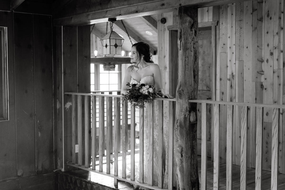 A bride on the lodge's upstairs balcony in black and white, bouquet in hand