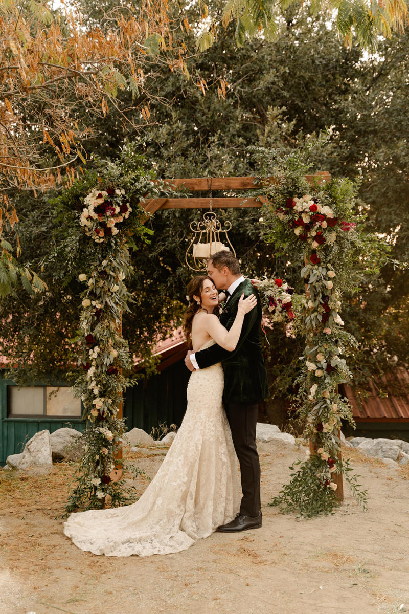 A couple's first kiss beneath the floral arbor outside the green lodge